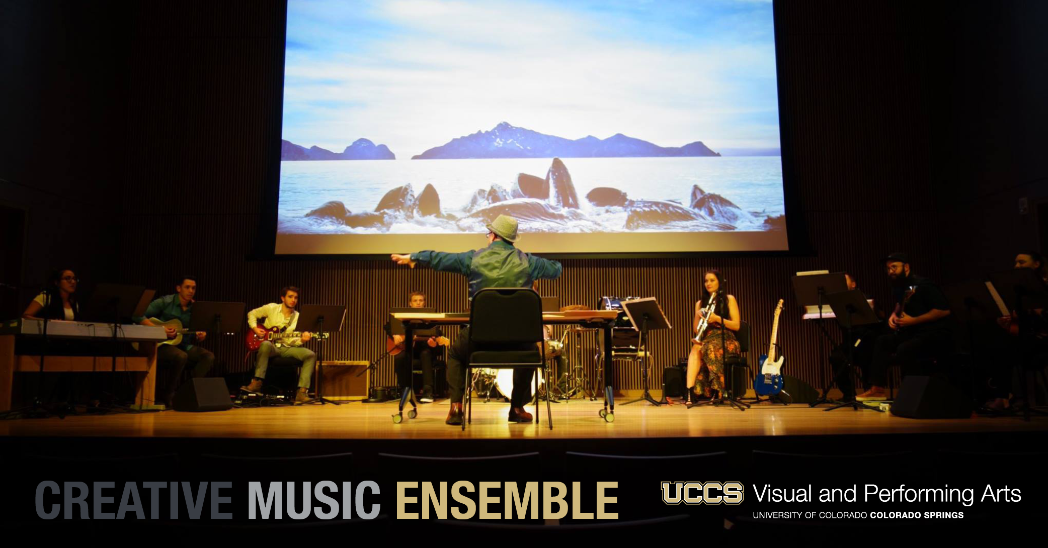glen whitehead directing the creative music ensemble on the chapman stage in front of a screen with a video of a whale's tail splashing in the ocean