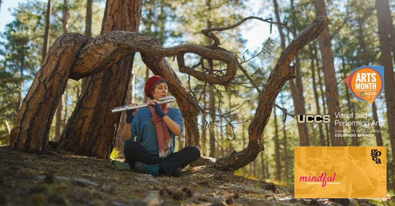 jane rigler sitting in front of a twisted tree playing the flute