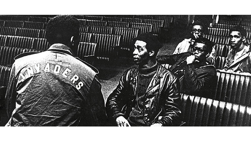 A picture of five young black men, wearing 60's-style jackets and sitting in pews of some sort. One has his back turned to the camera, and the word "INVADERS" can be seen on the back of his jacket.